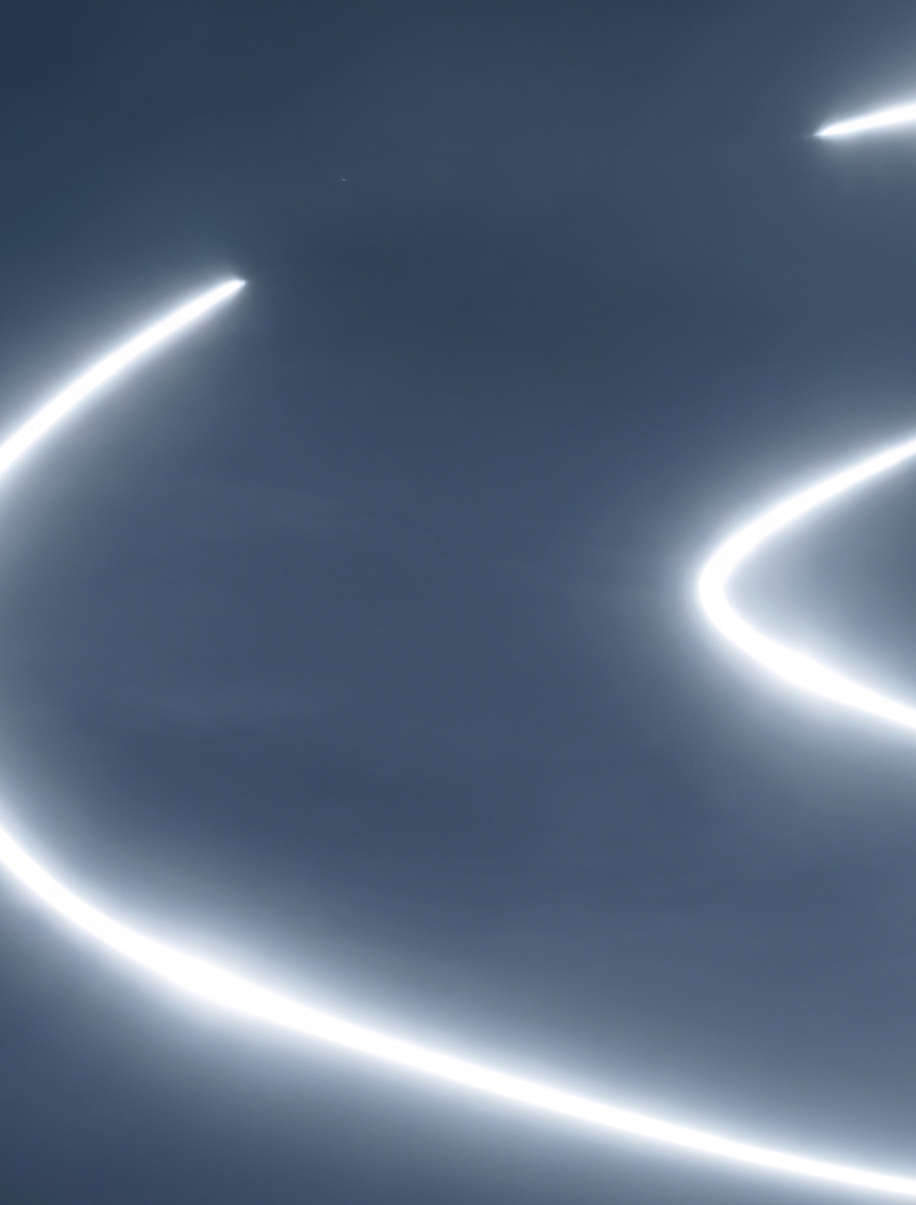 Long white light trails curving across a slate blue field.