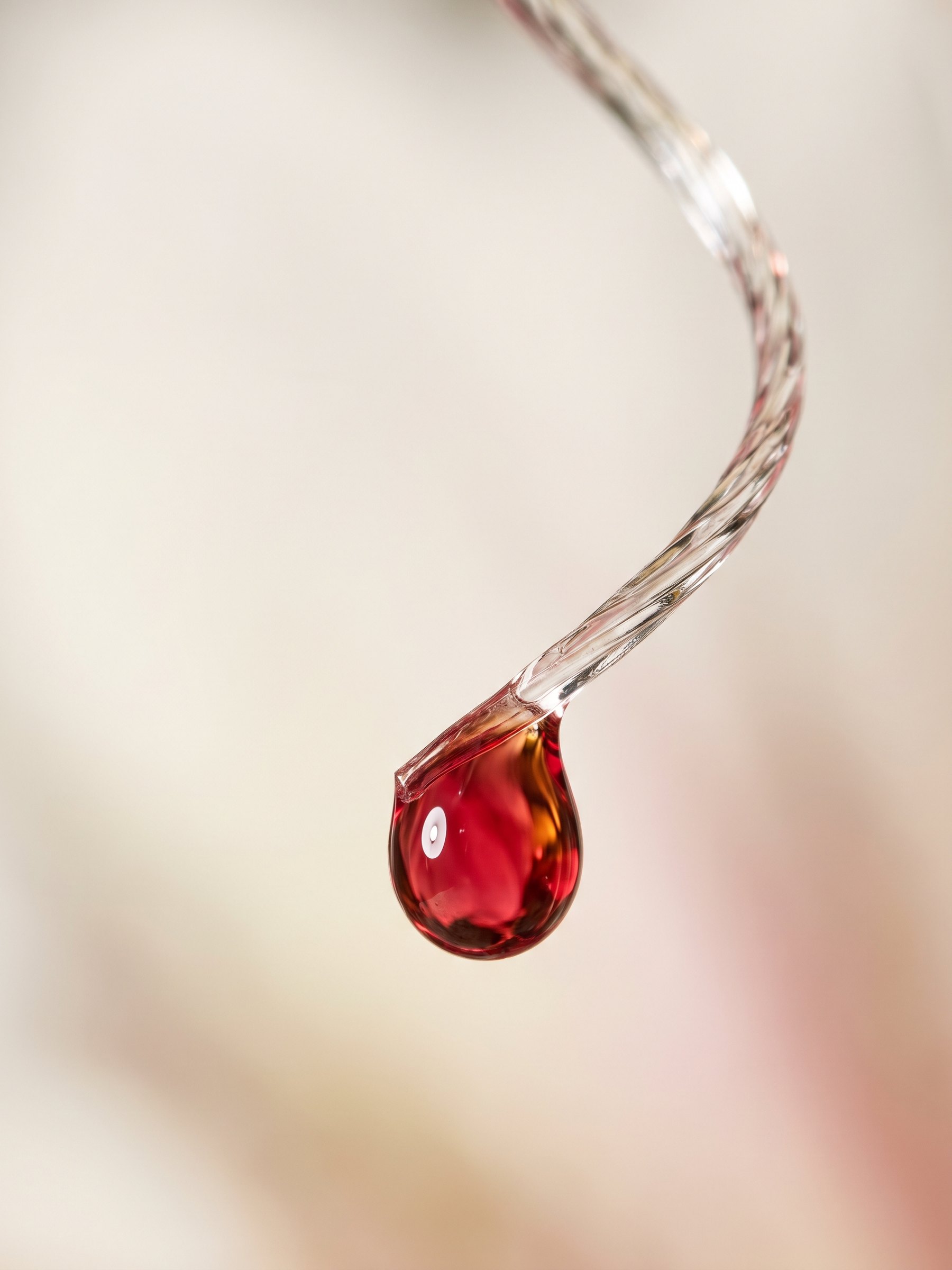 A crimson droplet hanging from a twisted clear strand on a soft cream field.