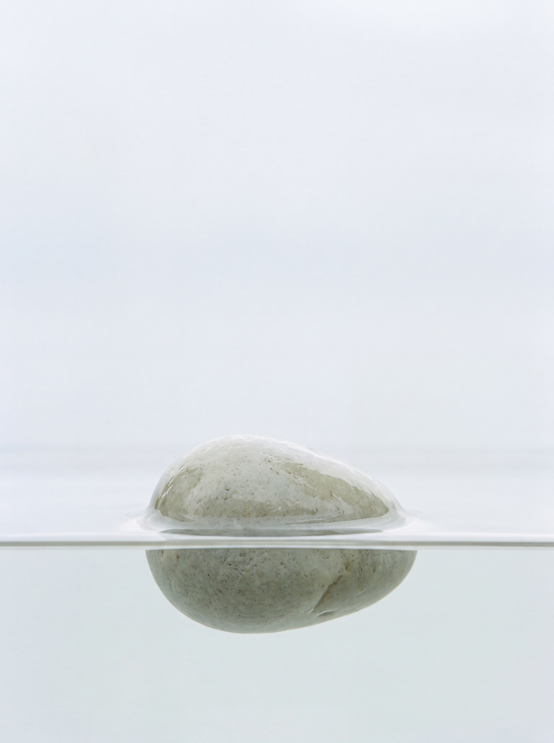 A pale stone resting at the surface of still water, with one clean waterline across the frame.